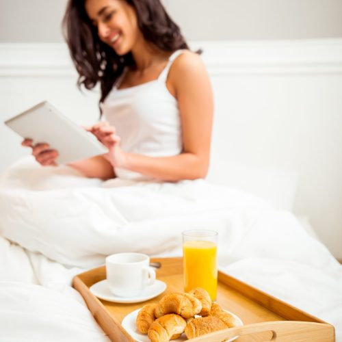 Beautiful girl in a white shirt using a tablet during breakfast in bed